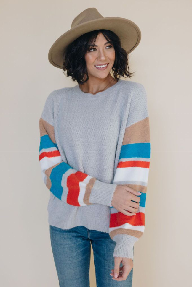 Light blue knit sweater with red, white and teal striped sleeves, ribbed hem