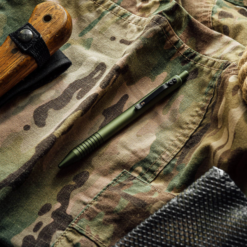 Olive green ballpoint pen with black accents and ridged grip, on camouflage fabric