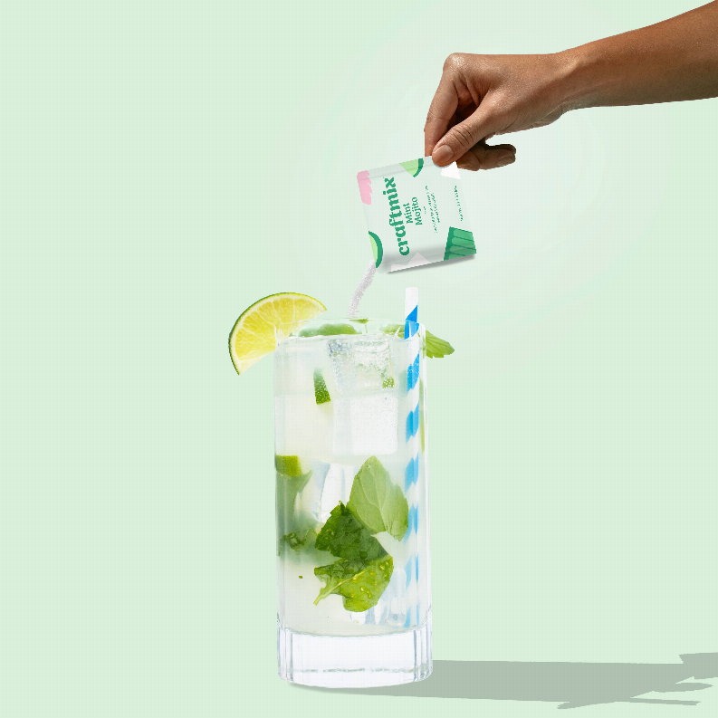Mint Mojito mixer packet being poured into a glass with ice, mint, and lemon