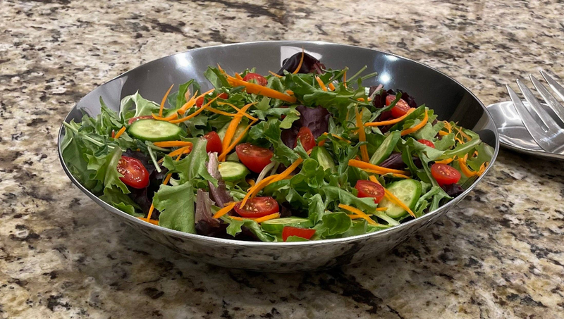Dark gray salad bowl with mixed greens, tomatoes, and carrots; fork beside it