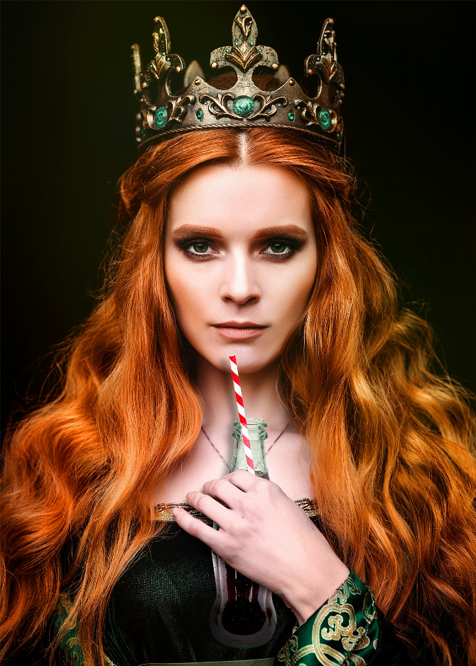 Glass wall art close-up of red-haired woman with gold crown and striped drink straw