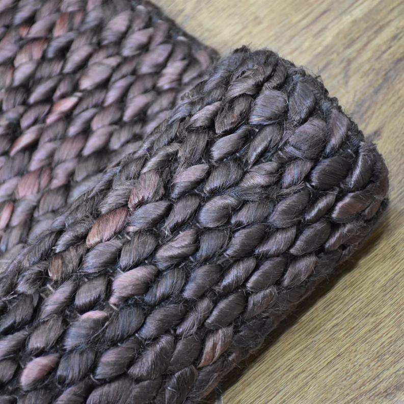 Hand-woven jute rug detail: chunky braided fibers in dark gray with muted rose accents