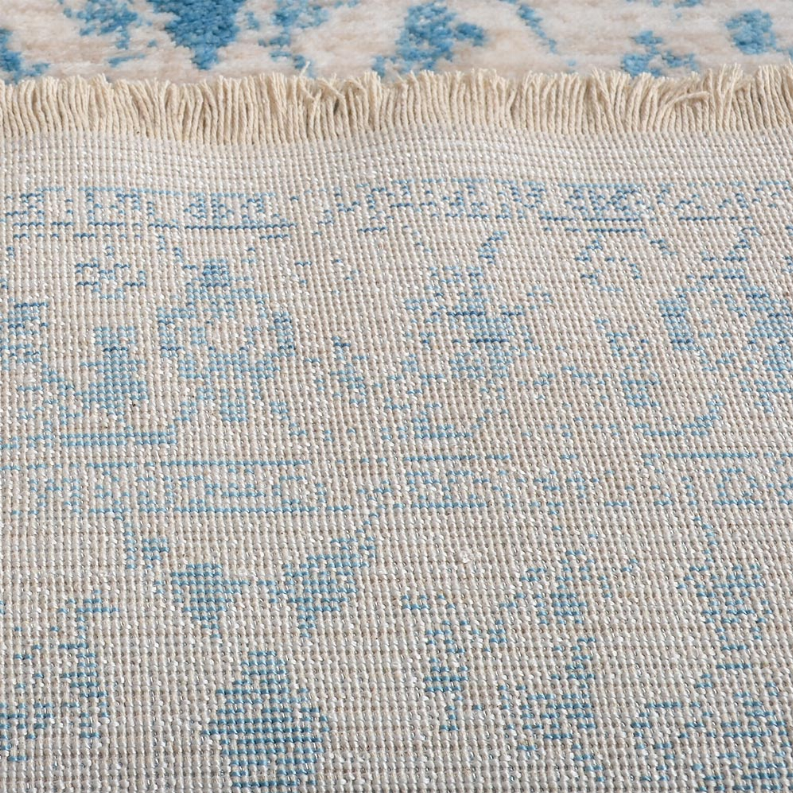 Rug close-up showing cream pile texture, scattered blue motifs, and short fringe.