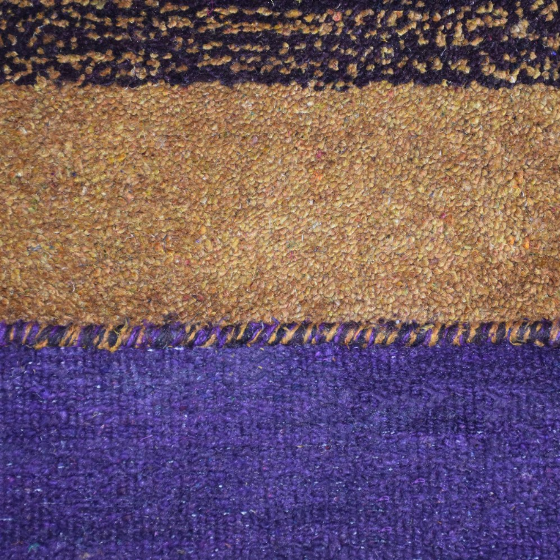Closeup of rug border showing tan speckled weave above purple pile