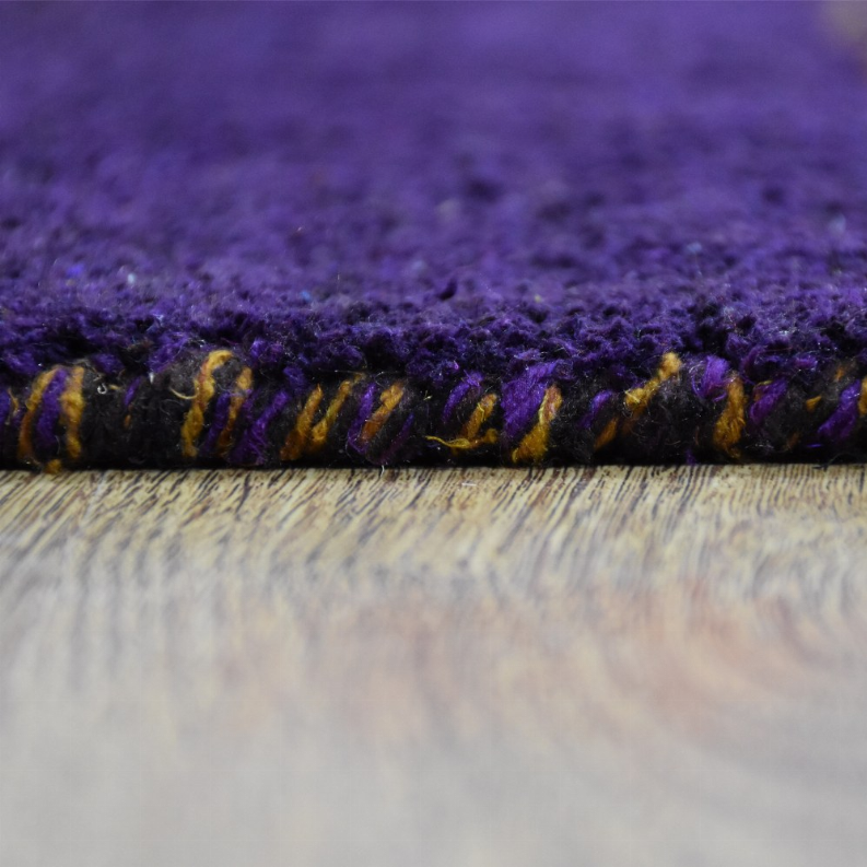 Edge closeup of purple area rug fringe with dark and gold threads