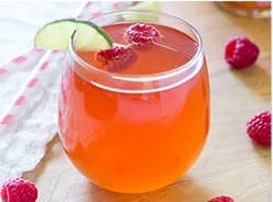 Raspberry-colored drink in glass with raspberries nearby