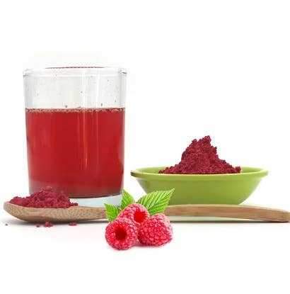 Freeze dried raspberry powder in green bowl with fresh raspberries and wooden spoon