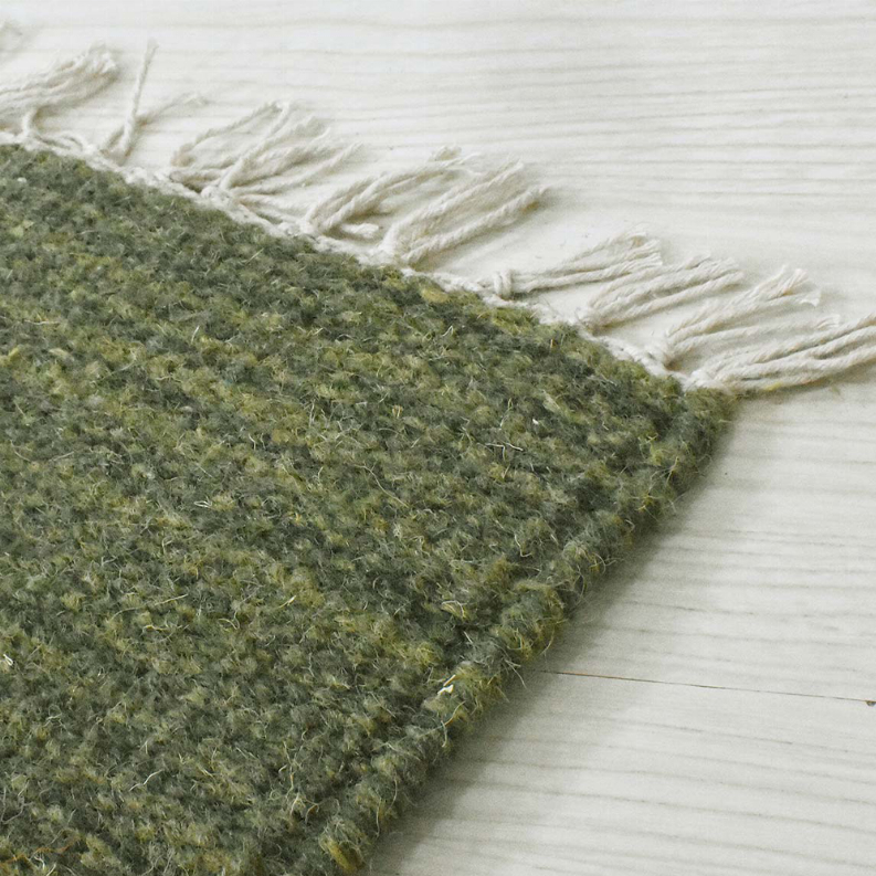 Olive green wool rug corner with white fringe and textured flat weave