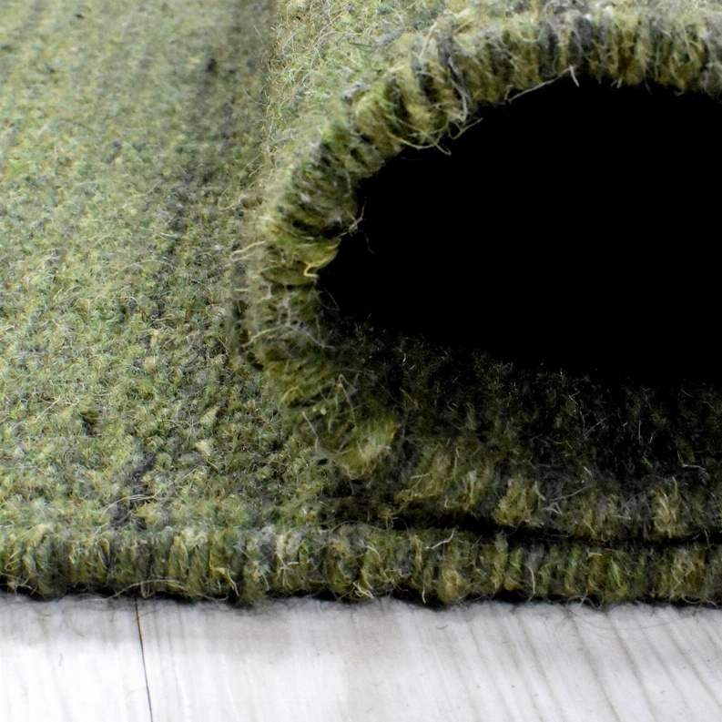 Olive green wool area rug edge showing dense fibers and light fringe along border