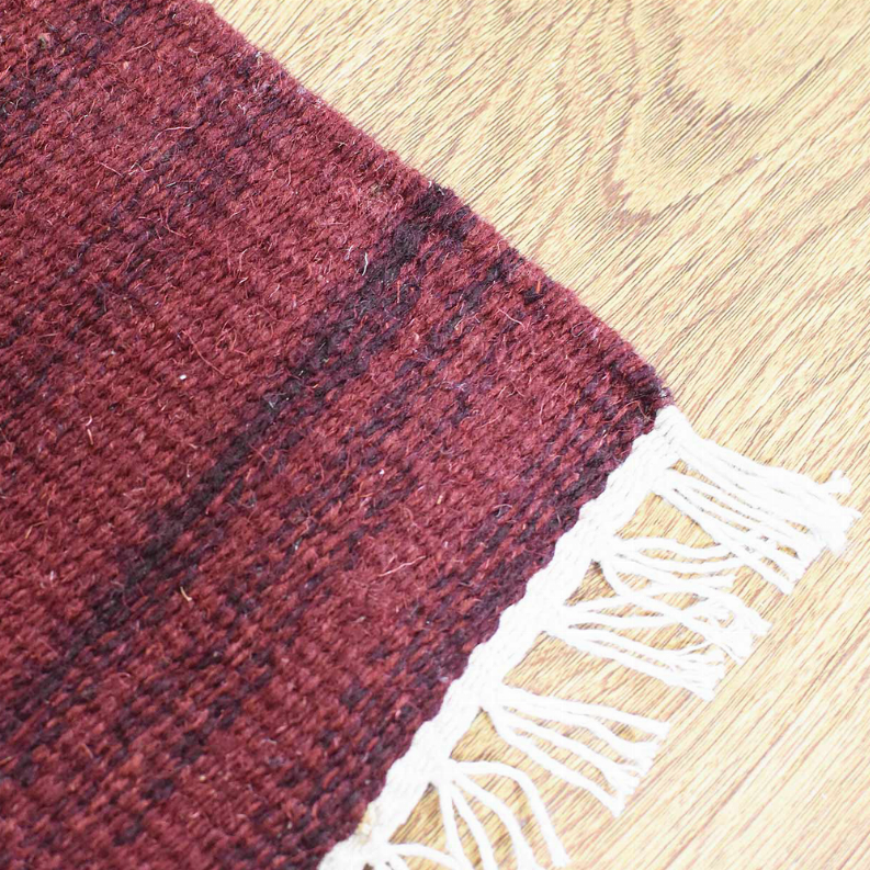 Burgundy wool rug corner with white fringe and off-white backing edge