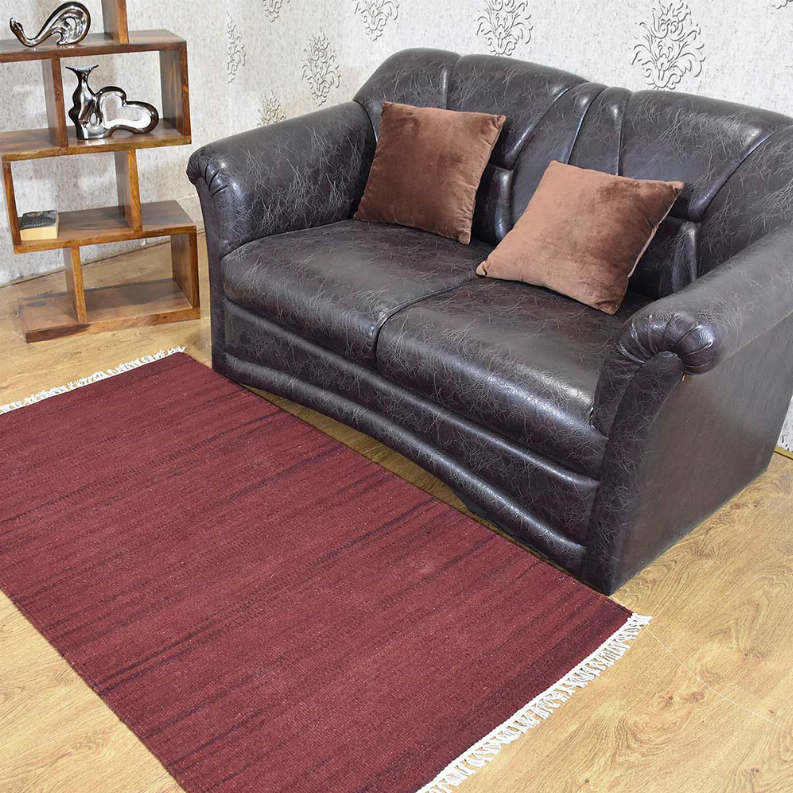 Burgundy wool kilim flatweave rug with fringe corners beneath a sofa and chairs