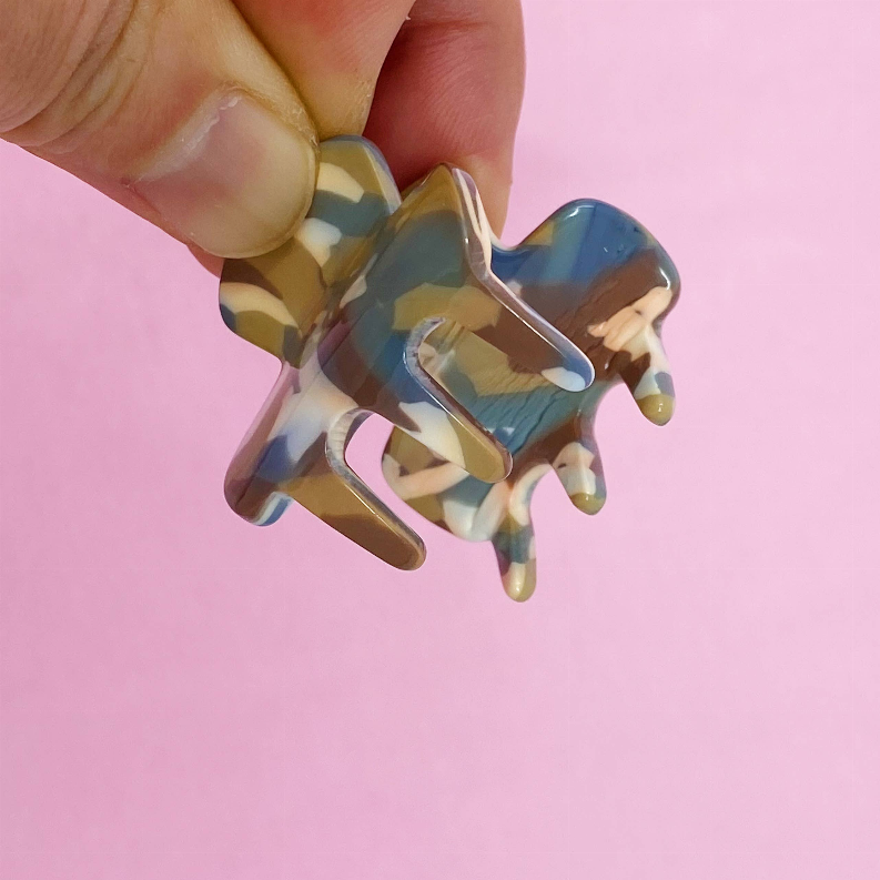 Mini marbled hair claw clip in beige and blue, held by fingers
