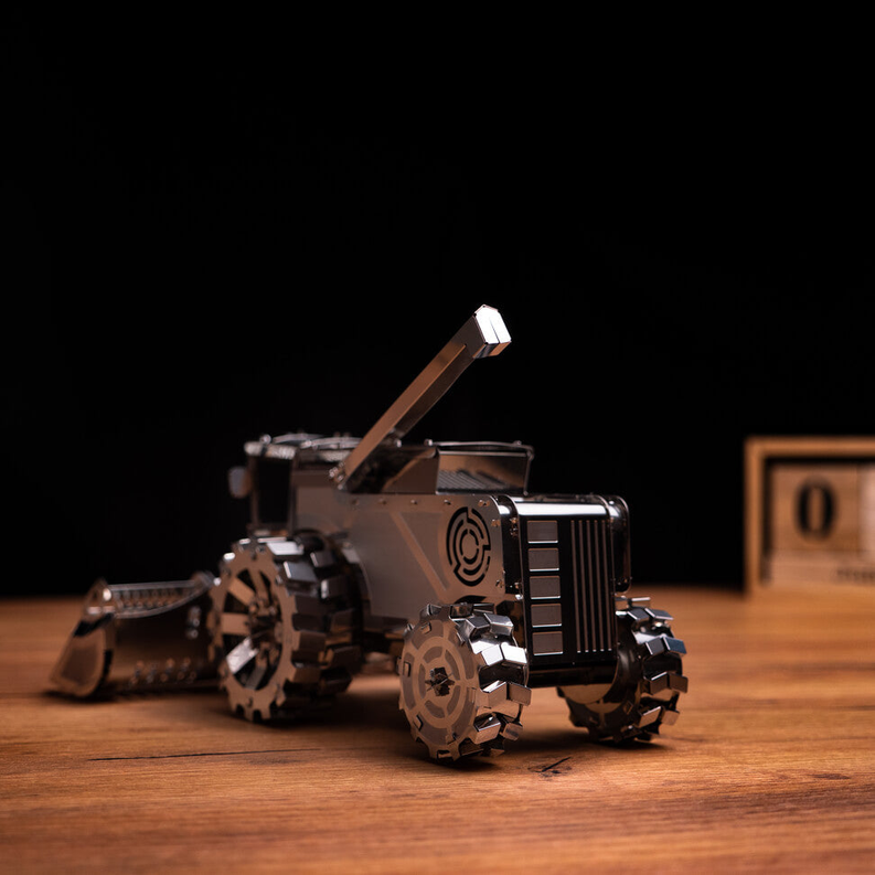 Metal harvester toy side view with raised arm and chunky wheels, bronze and silver.