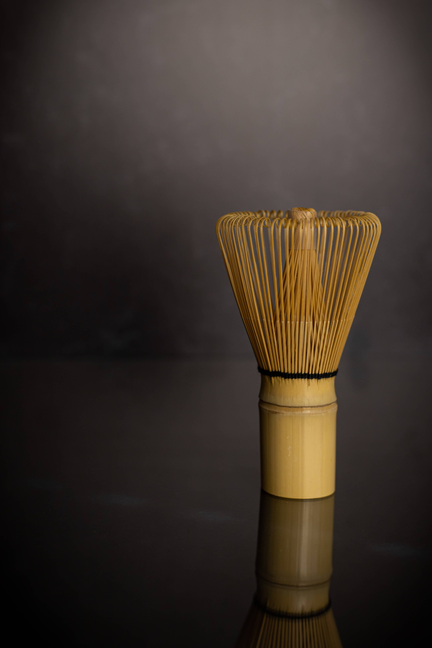 Bamboo matcha tea whisk on a reflective surface, wooden handle and tines