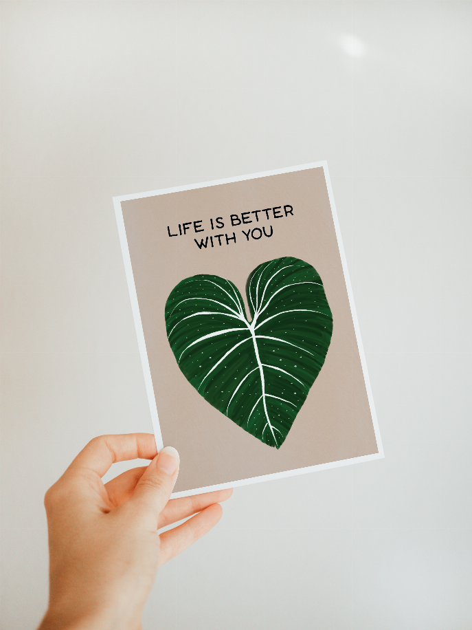 Hand holding printed greeting card with green leaf-heart and "LIFE IS BETTER WITH YOU"