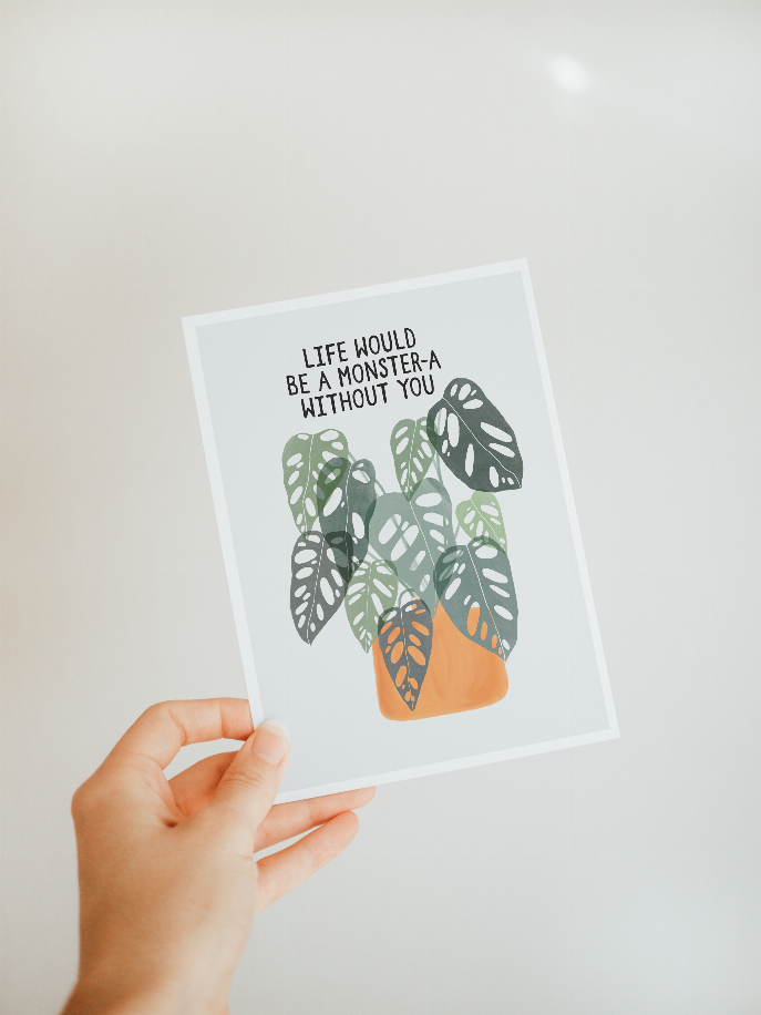 Close-up of hand holding framed monstera leaf wall art print with quote.