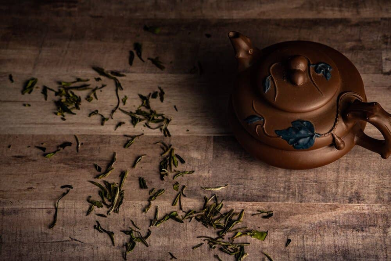 Brown teapot with blue flower accents and loose tea leaves on a wooden surface