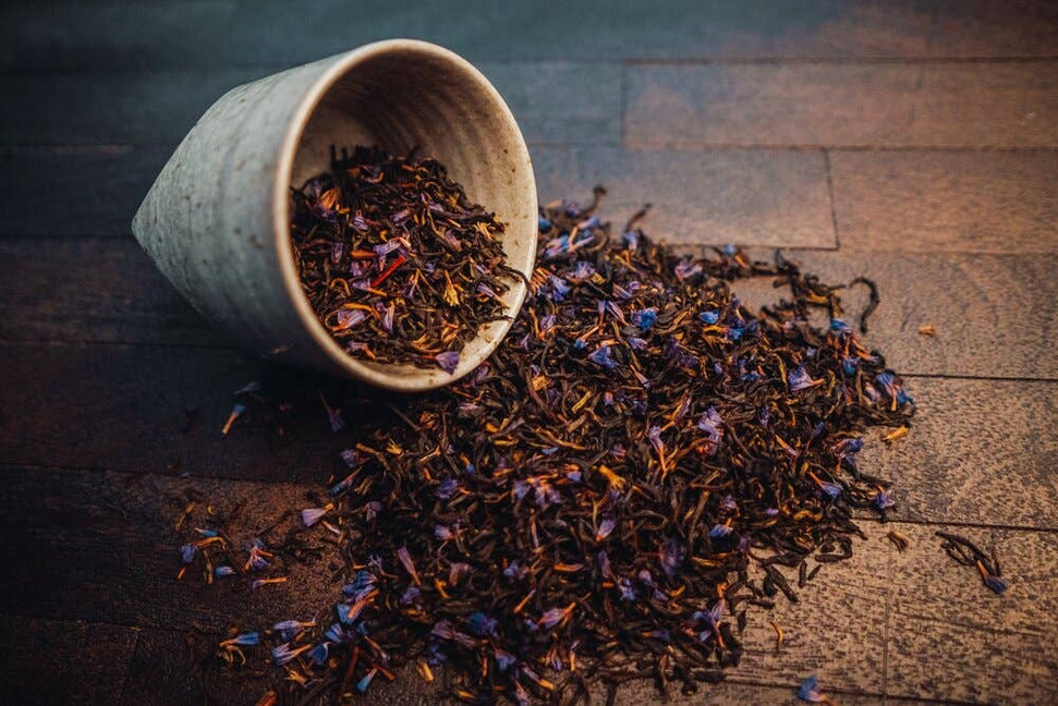 Earl Grey tea leaves spilled on table, with cup brimming beside them