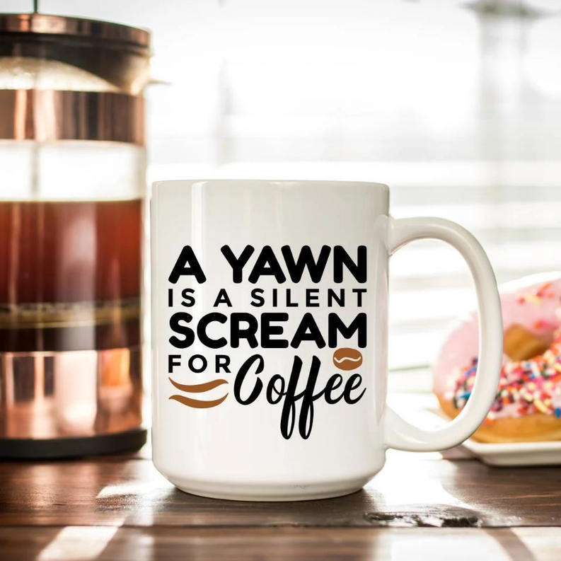 White coffee mug with black and brown text design: “A Yawn is a Silent Scream for Coffee”