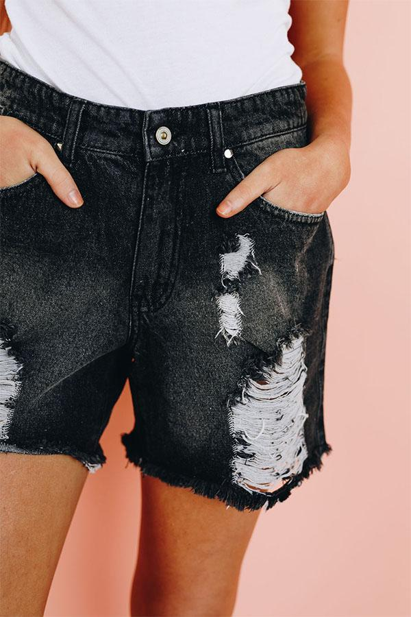 Black denim shorts with distressed front panel, frayed hem, button waist