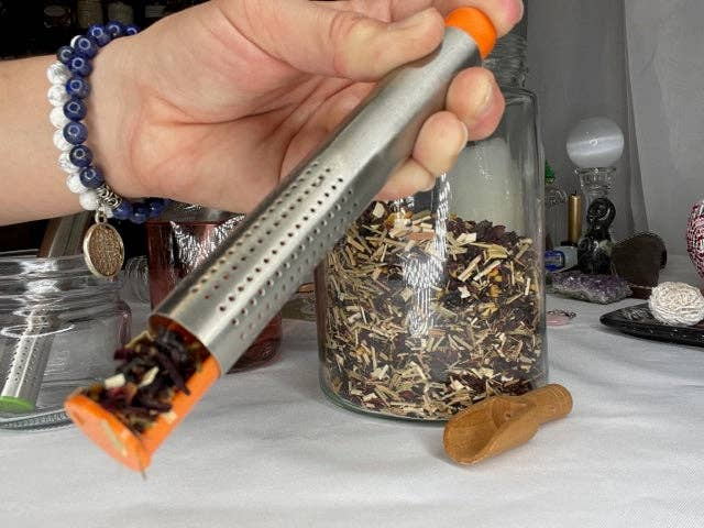 Tea stick infuser with perforated metal tube and orange end, held over loose leaf tea