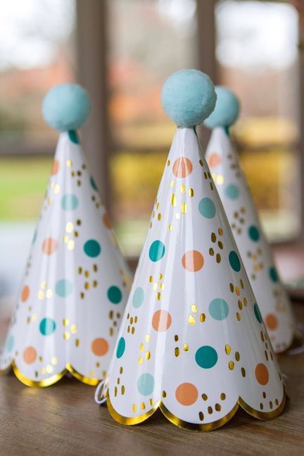 Two white cone party hats with light blue pom-poms and colorful polka dots