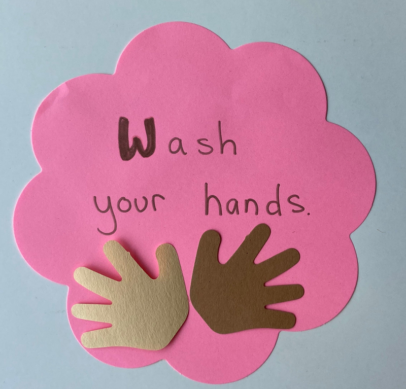 Pink flower cut-out with handprints and handwritten “Wash your hands” message