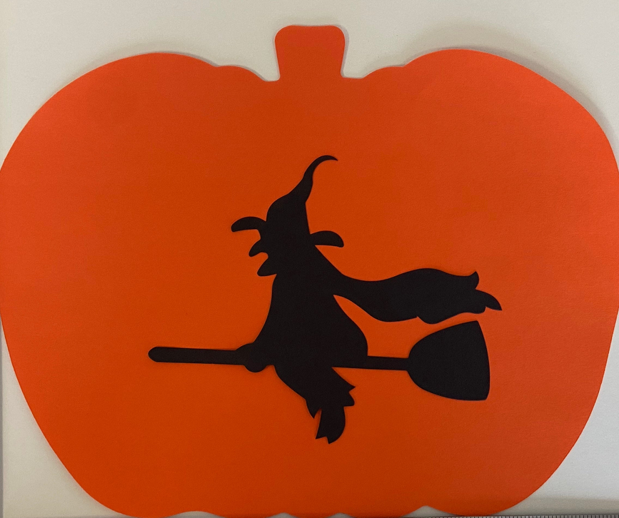 Orange pumpkin cut-out with black witch hat and broom silhouette