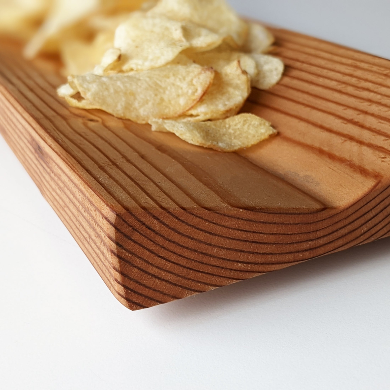 Wooden bowl board with grooves, topped with thin potato chips and crumbs