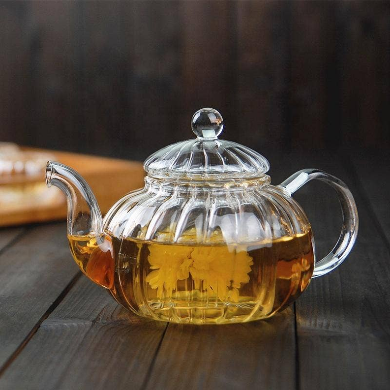Clear glass teapot with dome lid and side handles, filled with amber tea