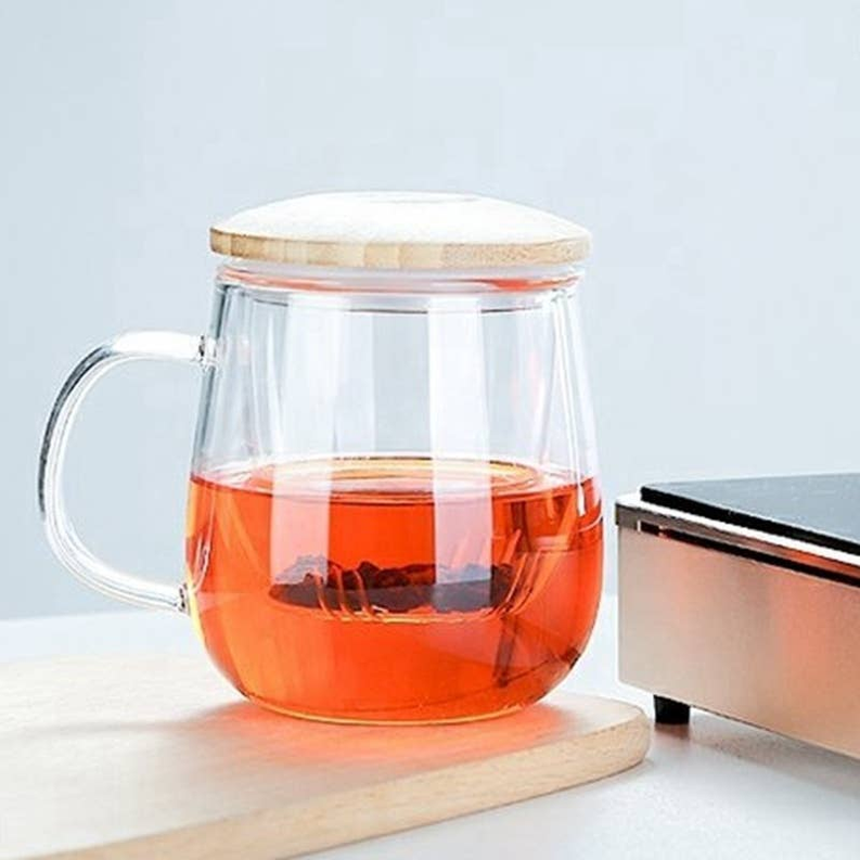 Glass teacup with bamboo lid and infuser, clear cup filled with amber tea on base