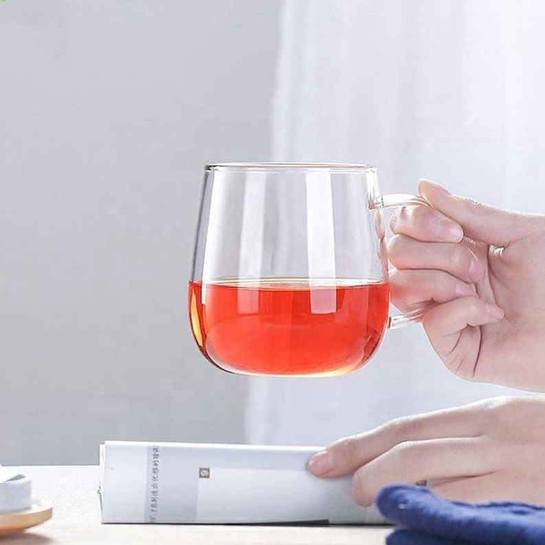 Glass teacup with infuser, clear cup in hand with amber tea; bamboo lid not visible