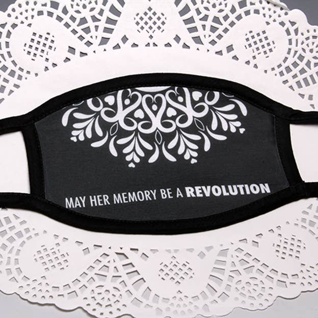 Black face mask with white floral print and text "May her memory be a revolution"