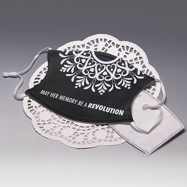 Black face mask with white floral print, slogan "May her memory be a revolution", ear loops
