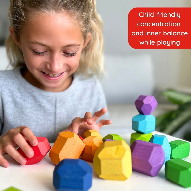 Child hands reaching among multicolor wooden balancing stones arranged on the floor