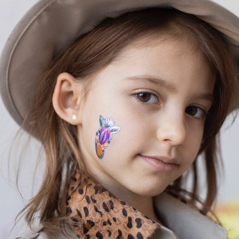 Child with a safari temporary tattoo on cheek featuring a colorful lion-head design