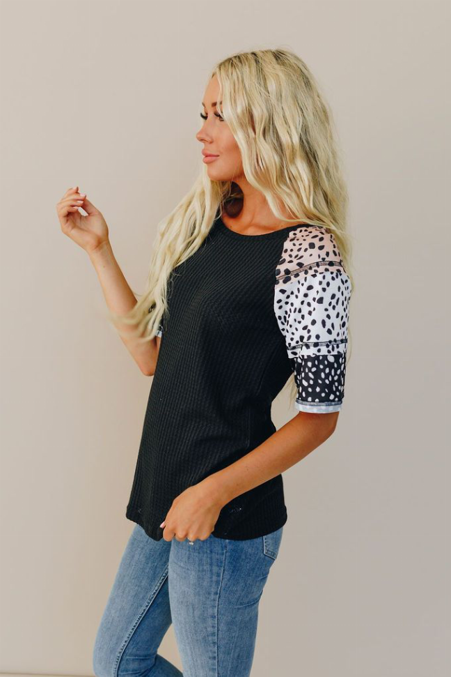 Black knit top with white spotted raglan sleeves, side view.