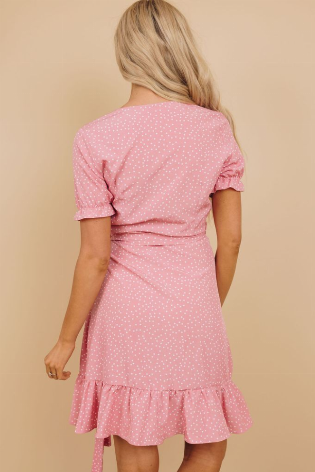 Pink dotted wrap dress back view with gathered waist and tiered ruffle skirt.