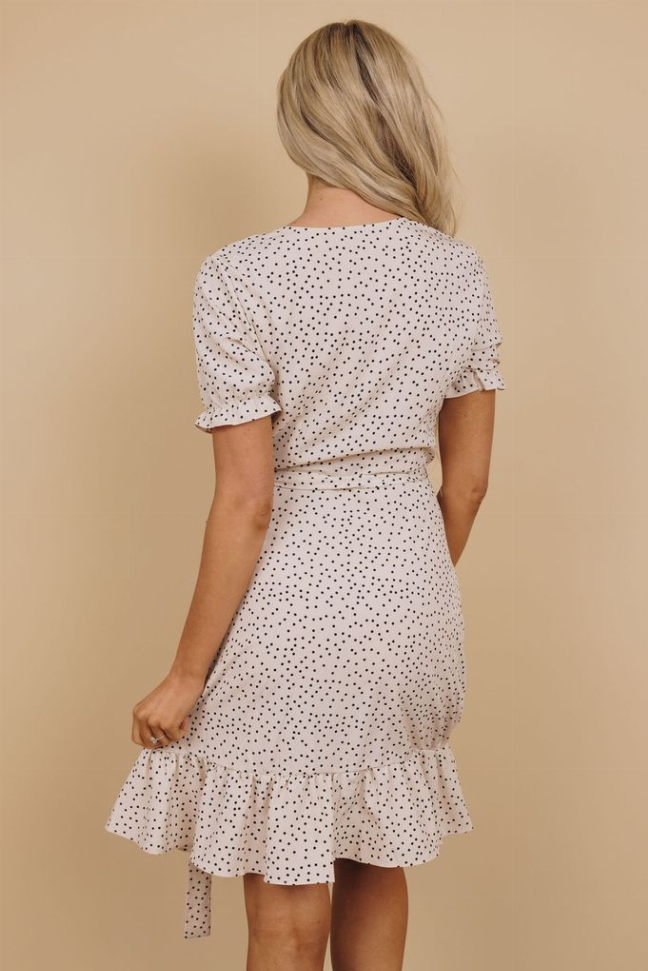 Back view of white dotted wrap dress with short sleeves, tie waist, and ruffled tiered hem