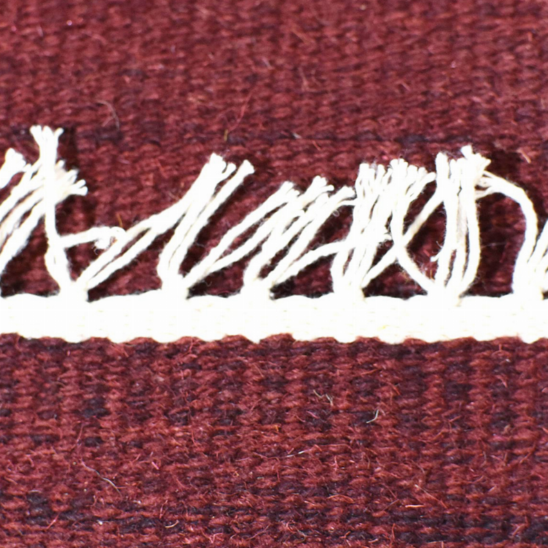 Burgundy wool rug with prominent off-white fringe strip across the edge