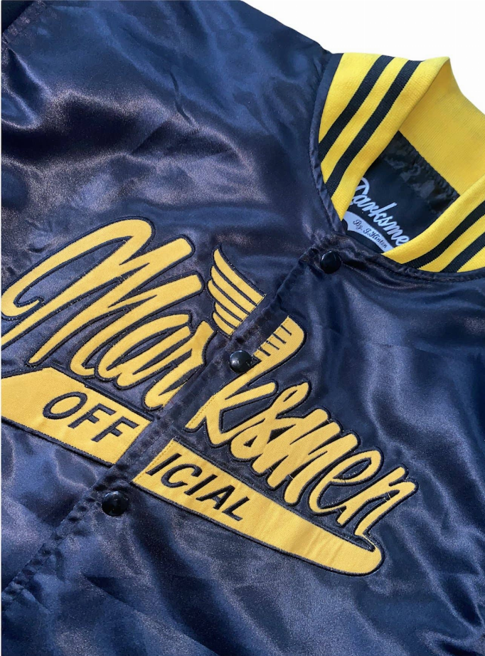 Close-up of dark blue silk bomber jacket with yellow striped collar and scripted front logo