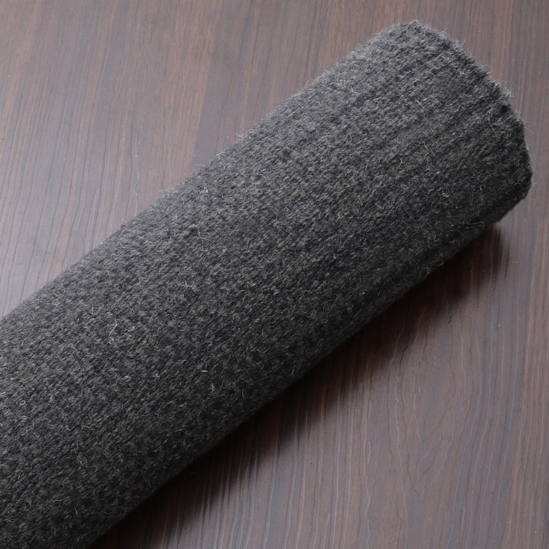 Rolled dark gray wool rug showing flat weave thickness and dense texture