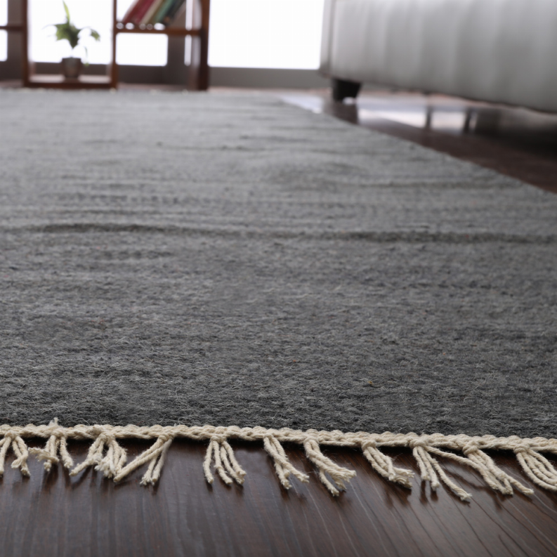 Dark gray wool area rug with flat weave texture and cream fringe trim