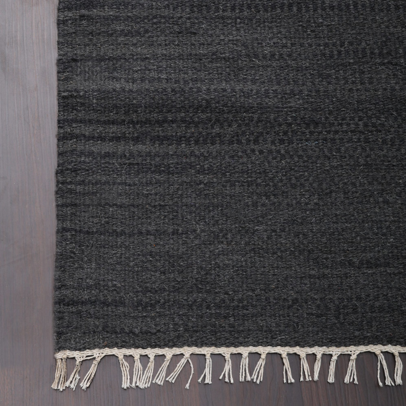Dark gray wool kilim rug edge with cream fringe along the border
