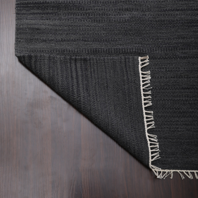 Dark gray wool flatweave kilim rug corner with stitched fringe border