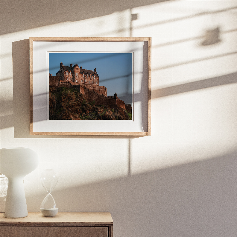 Framed castle print with light wood border and dark fortress over rocky ground.