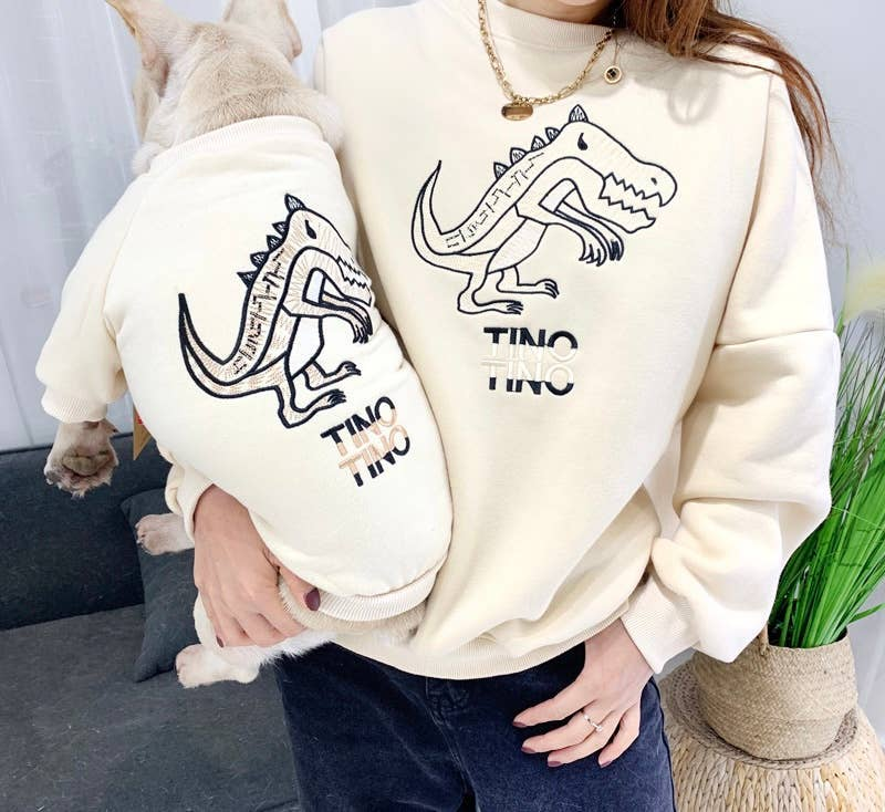 Cream sweatshirt and pet hoodie with blue dinosaur outline graphic, owner wearing