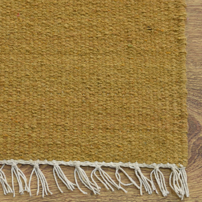 Solid mustard wool rug close-up with white fringed border