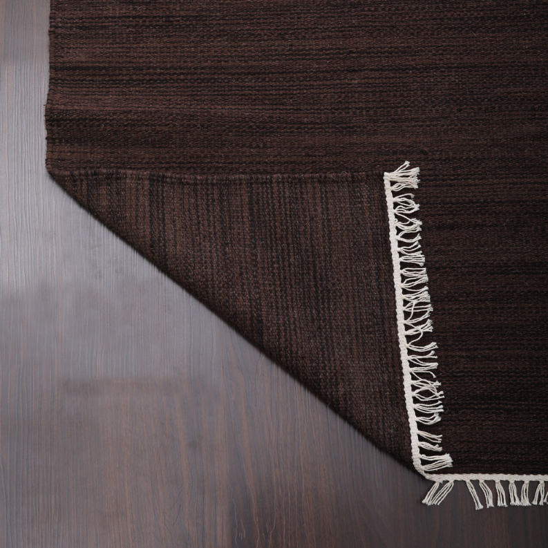 Dark brown wool rug corner detail with woven texture and white fringe