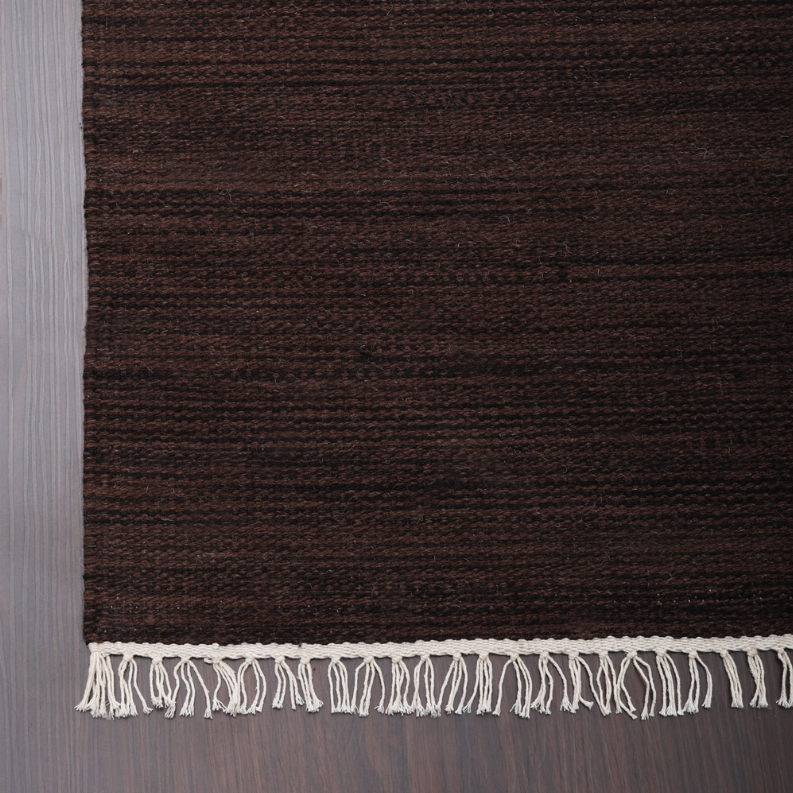 Dark brown wool kilim rug with short fringe trim along the bottom edge